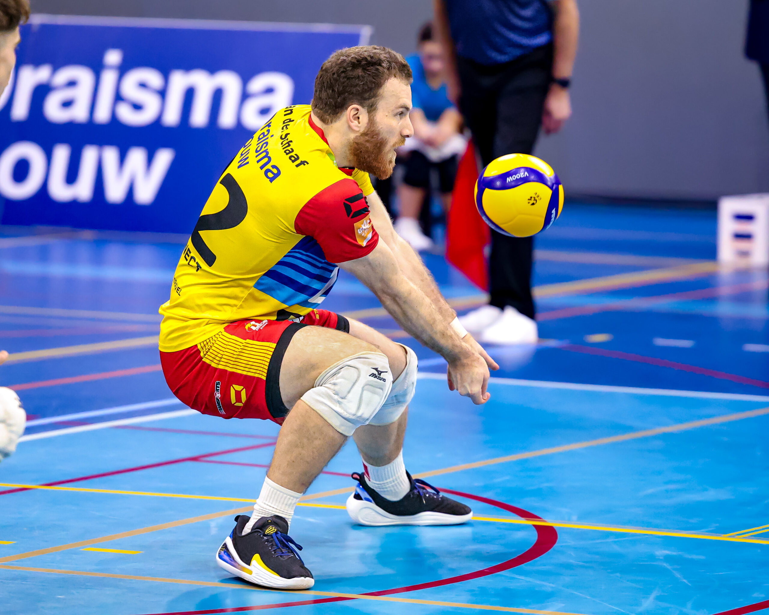 Volleyballer in actie tijdens een wedstrijd. Focus op de bal en de speler in geel-rood shirt. Professioneel volleybal.