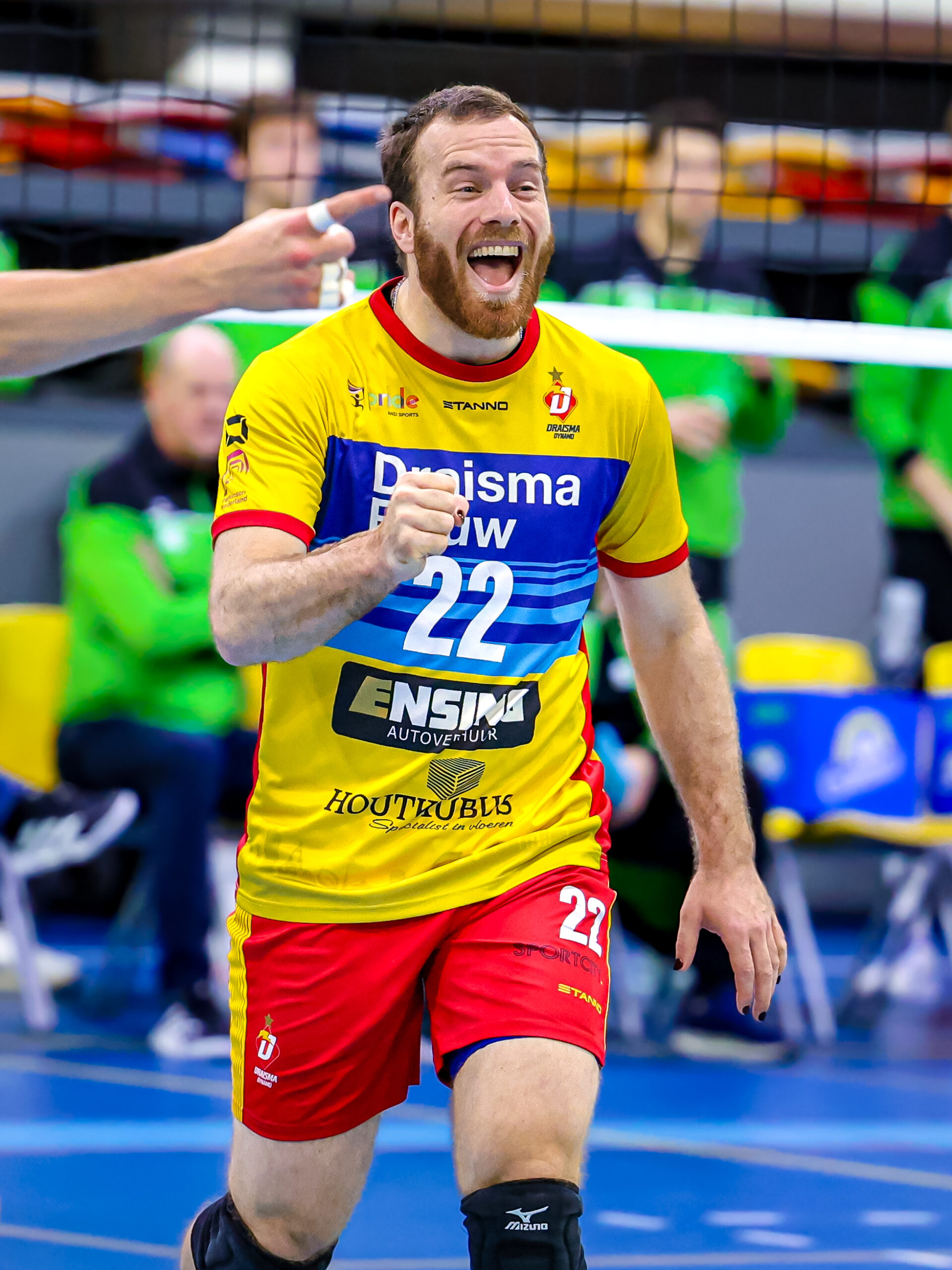 Volleyballer in actie! Enthousiaste speler met geel-rood shirt nummer 22 juicht tijdens een volleybalwedstrijd. Competitie en sportiviteit in beeld.