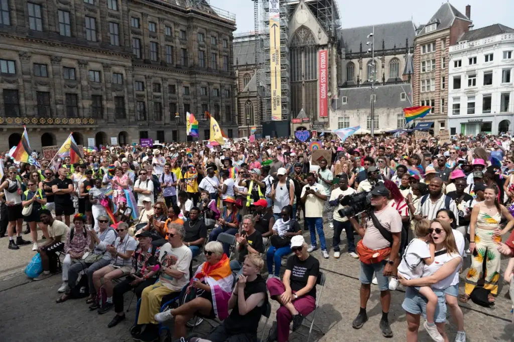 Drukte tijdens de Pride Walk in Amsterdam, met kleurrijke vlaggen en feestende mensen op de Dam. Viering van diversiteit en inclusie.